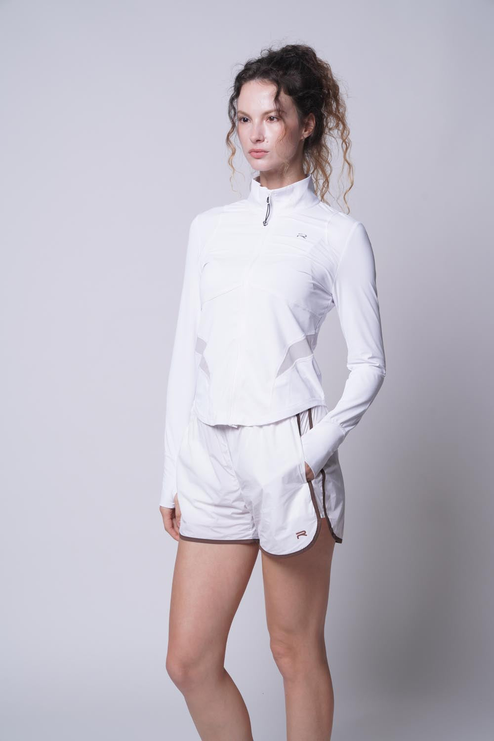 Female model wearing the white Ramsports Court Sculpt Full-Zip Jacket looking away from the camera with her left hand in the pocket
