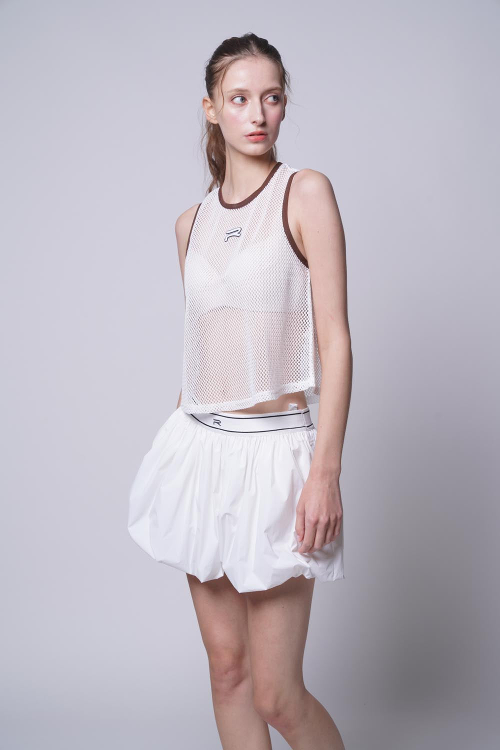 Female model standing sideways wearing Ramsports Court Flow Scoop Tank in white
