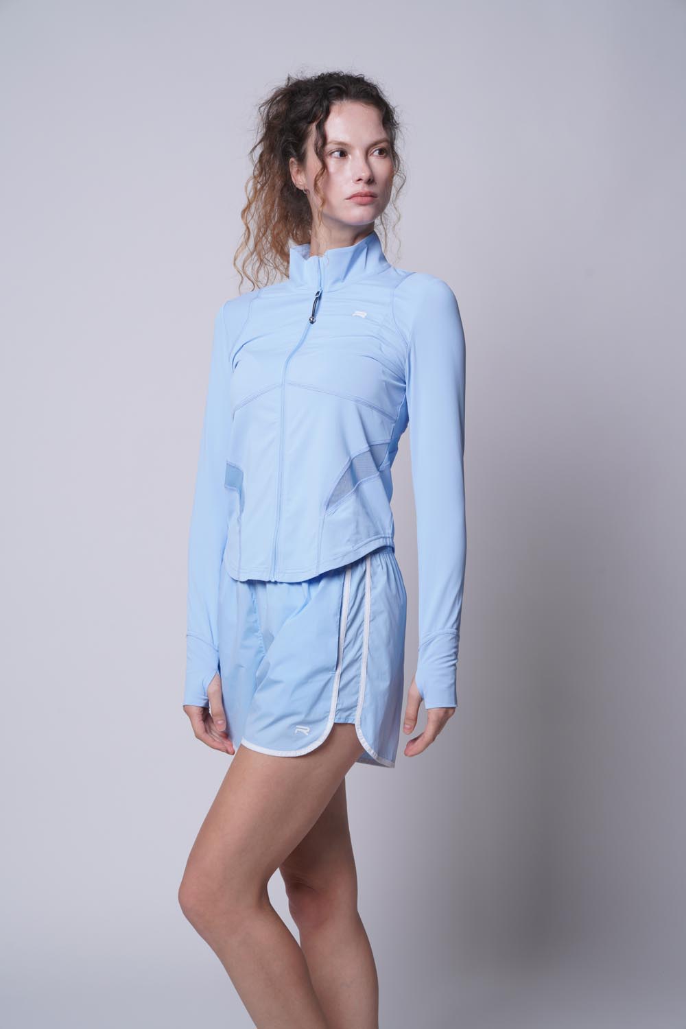 Female model looking away from the camera while wearing a blue Ramsports Flow Panel Split-Hem Short and a blue longsleeves