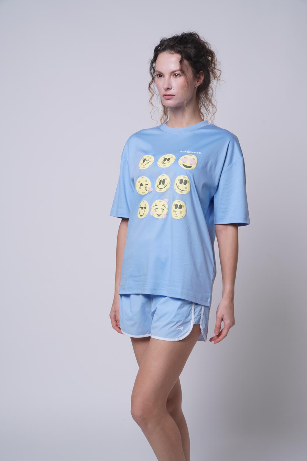 Female model standing sideways wearing Ramsports Court Moods Icon Grid T-shirt in blue