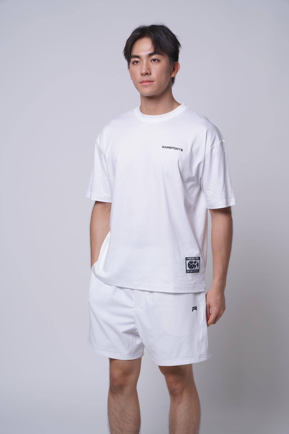 Male model wearing a white Ramsports Blueprint Back Graphic tee with white shorts, hand in pocket