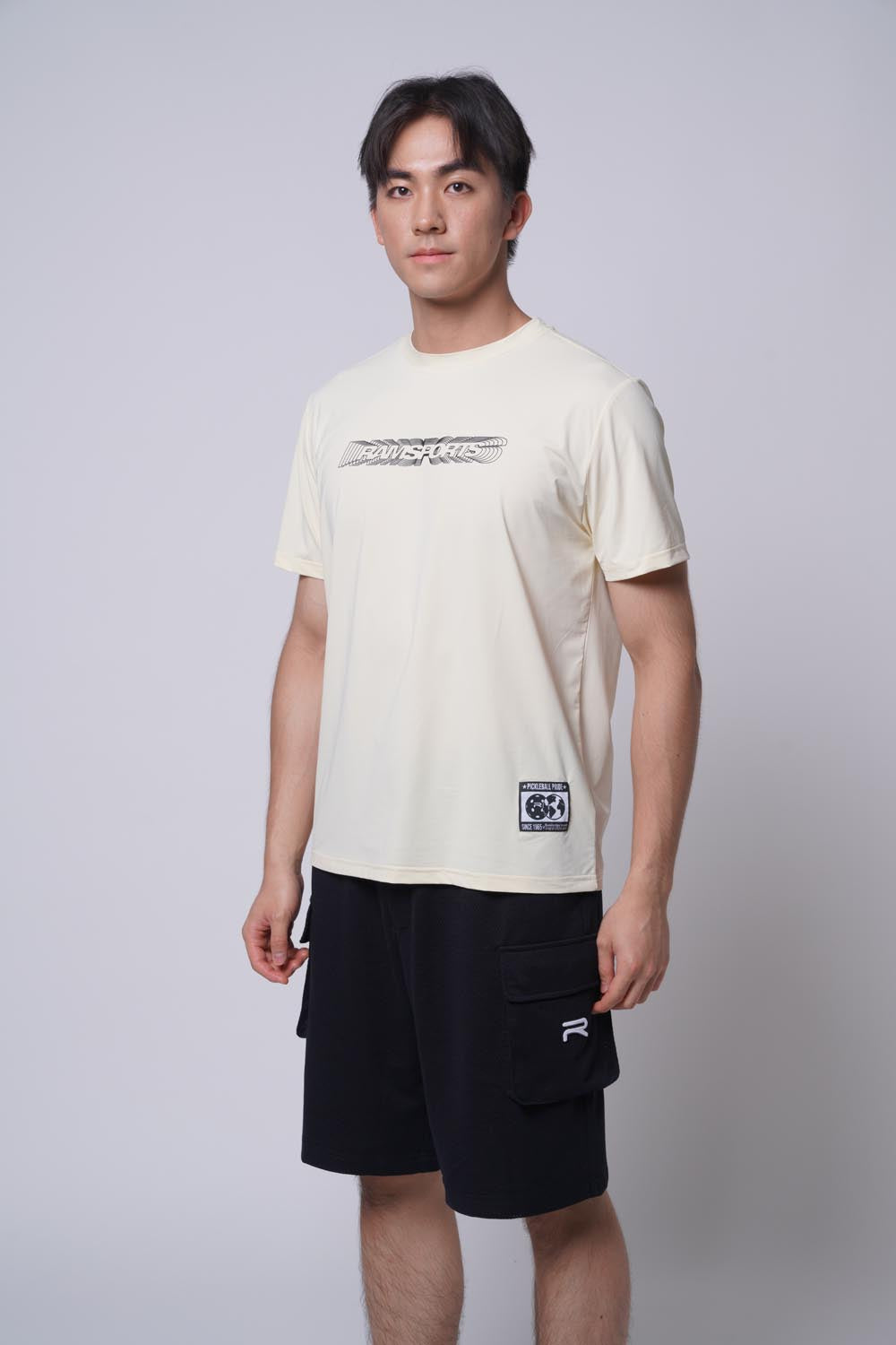 Male model wearing the beige Ramsports Playbook Court Diagram tee against a gray background, looking directly at the camera