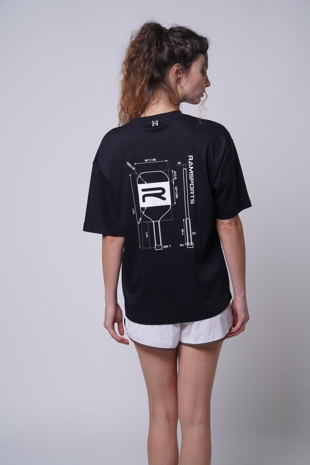 Female model facing away as she's wearing the Ramsports Flow Panel Split-Hem Short in white and matching black shirt.