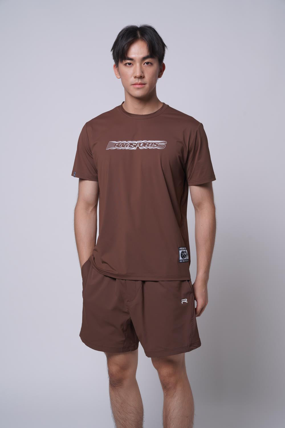 Male model standing with round top, with one hand on his pocket as he's wearing the Ramsports MatchDay Core Short in brown