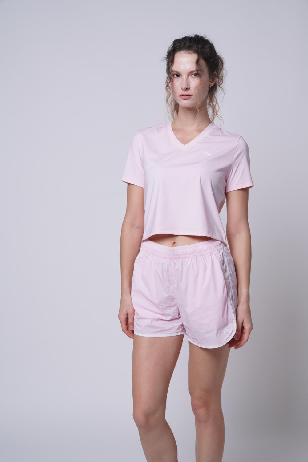 Female model in a pink Ramsports Keyhole Back Crop, standing straight, right leg slightly bent, hands at sides, looking away.