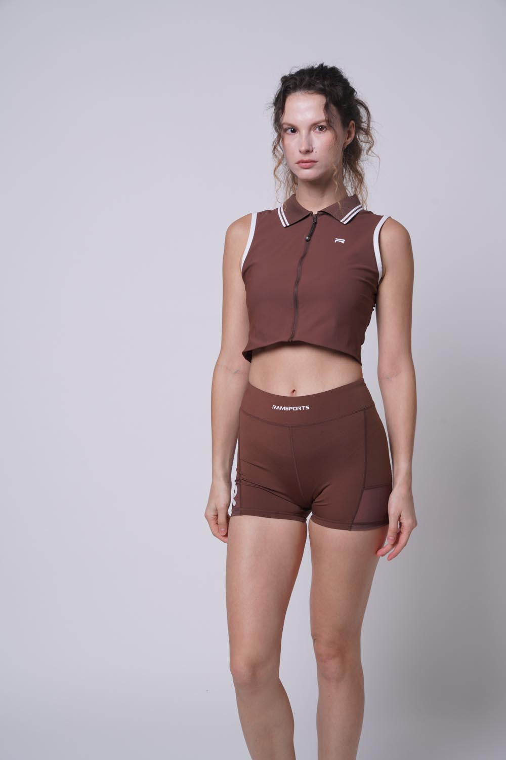 female model wearing a brown Ramsports Serve Zip Fitted Shorts set on a white background