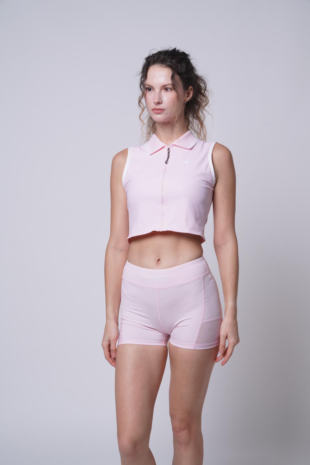 Female model modeling a pink Ramsports Serve Zip Fitted Shorts, facing the camera with gaze to the side.