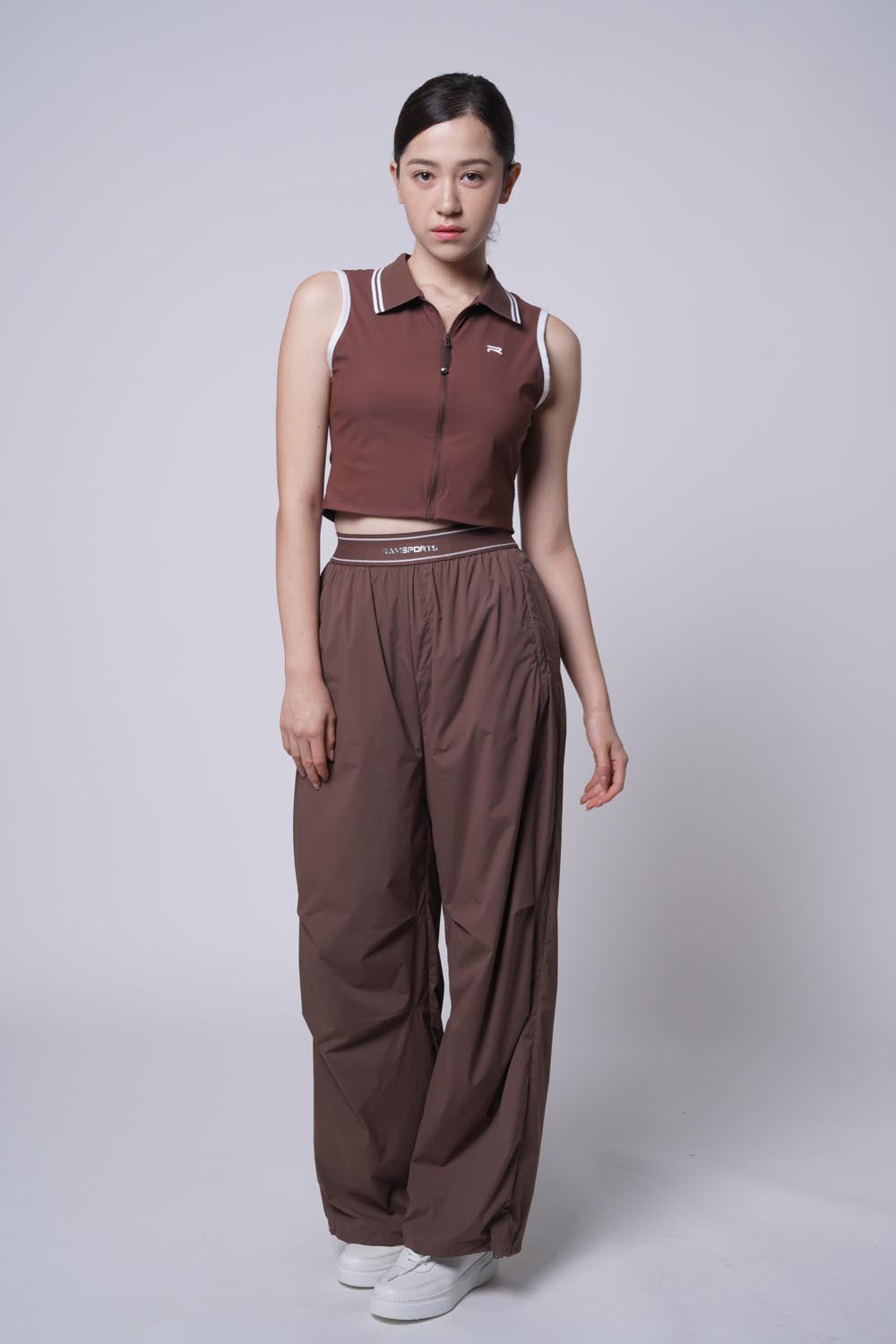 asian female model wearing Ramsports serve zip crop polo and a Court Sculpt Track Pants in brown
