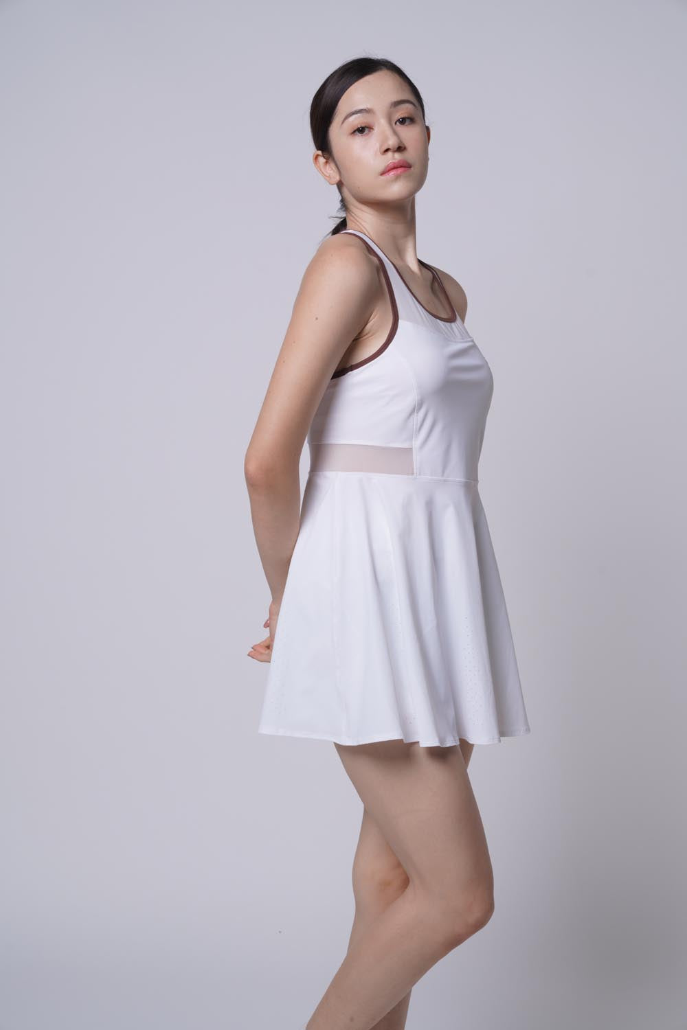 Asian female model posing on her right sideways as she's wearing a white Ramsports Racer Flare Dress.