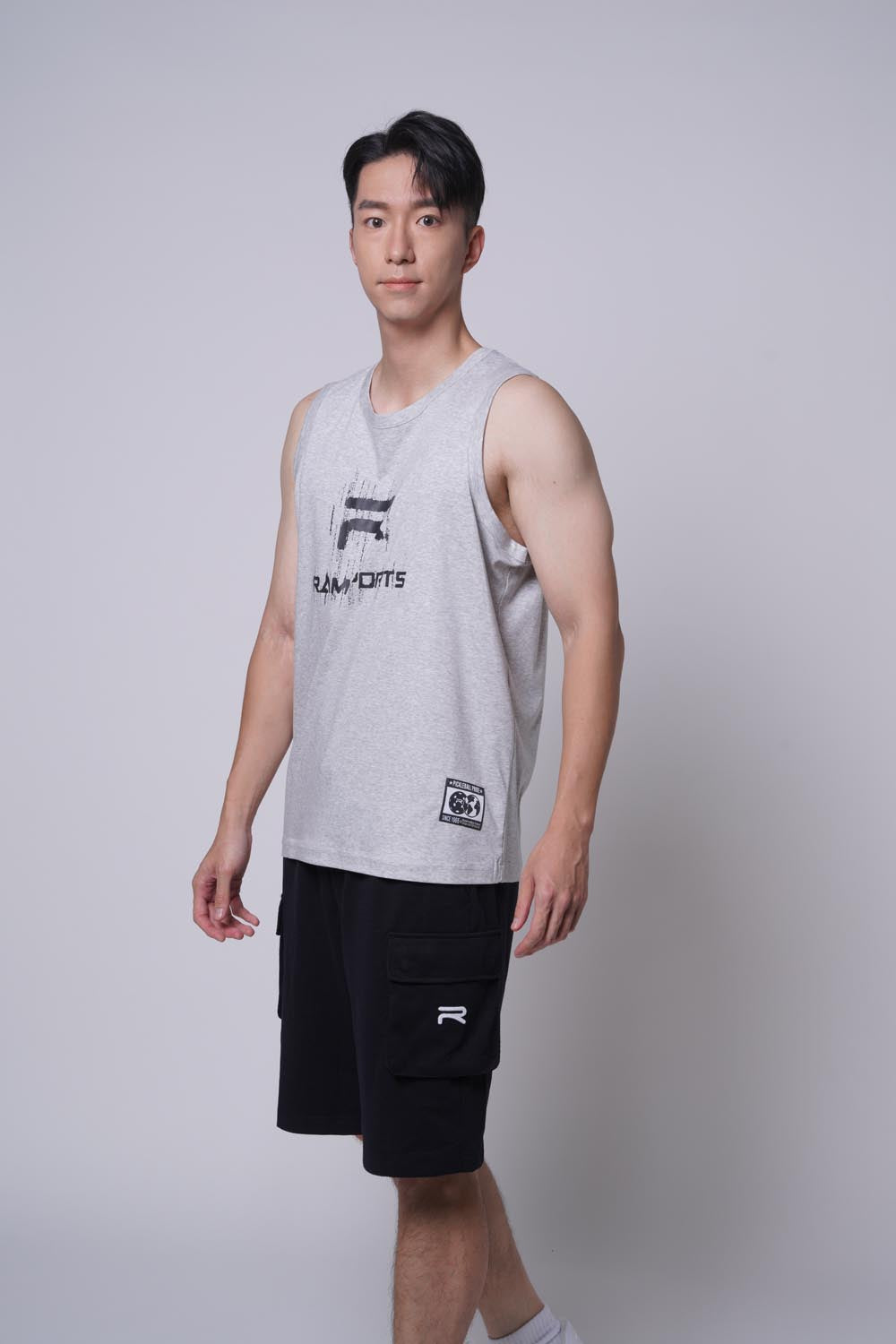 Asian male model standing sideways as if he's walking, wearing Ramsports repMark tank in gray