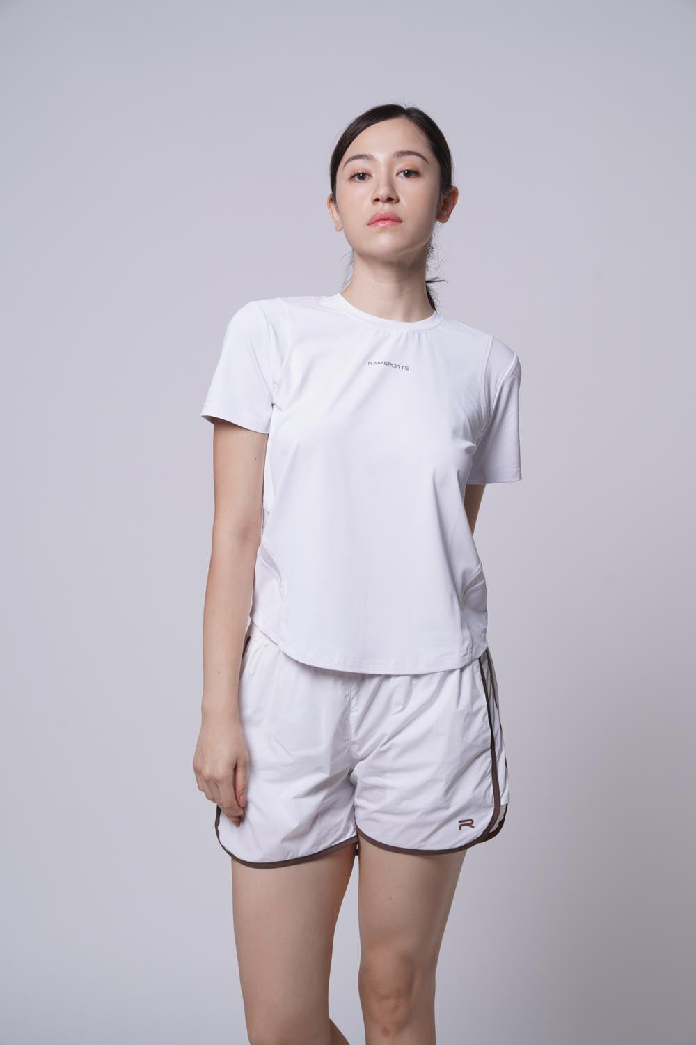 Asian female model with her chin raised, wearing a white Ramsports Flow Panel Crew Tee.