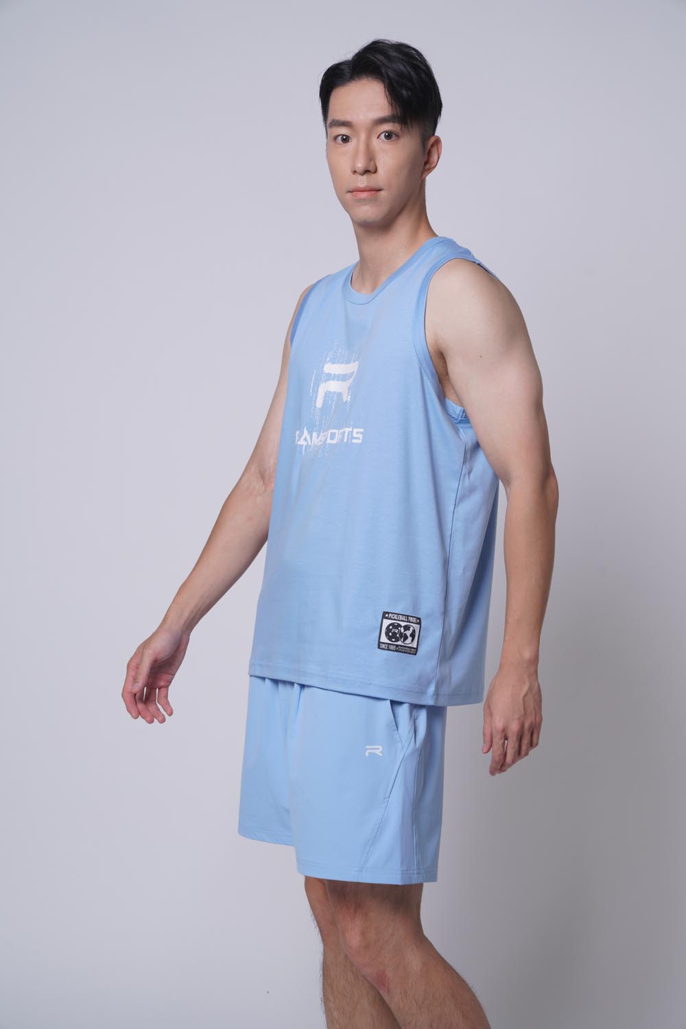 Asian male model looking at the camera, standing sideway as he's wearing Ramsports repMark tank in blue