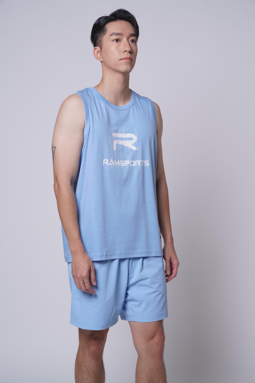 Asian male model looking at the camera, standing right view wearing Ramsports repMark tank in blue