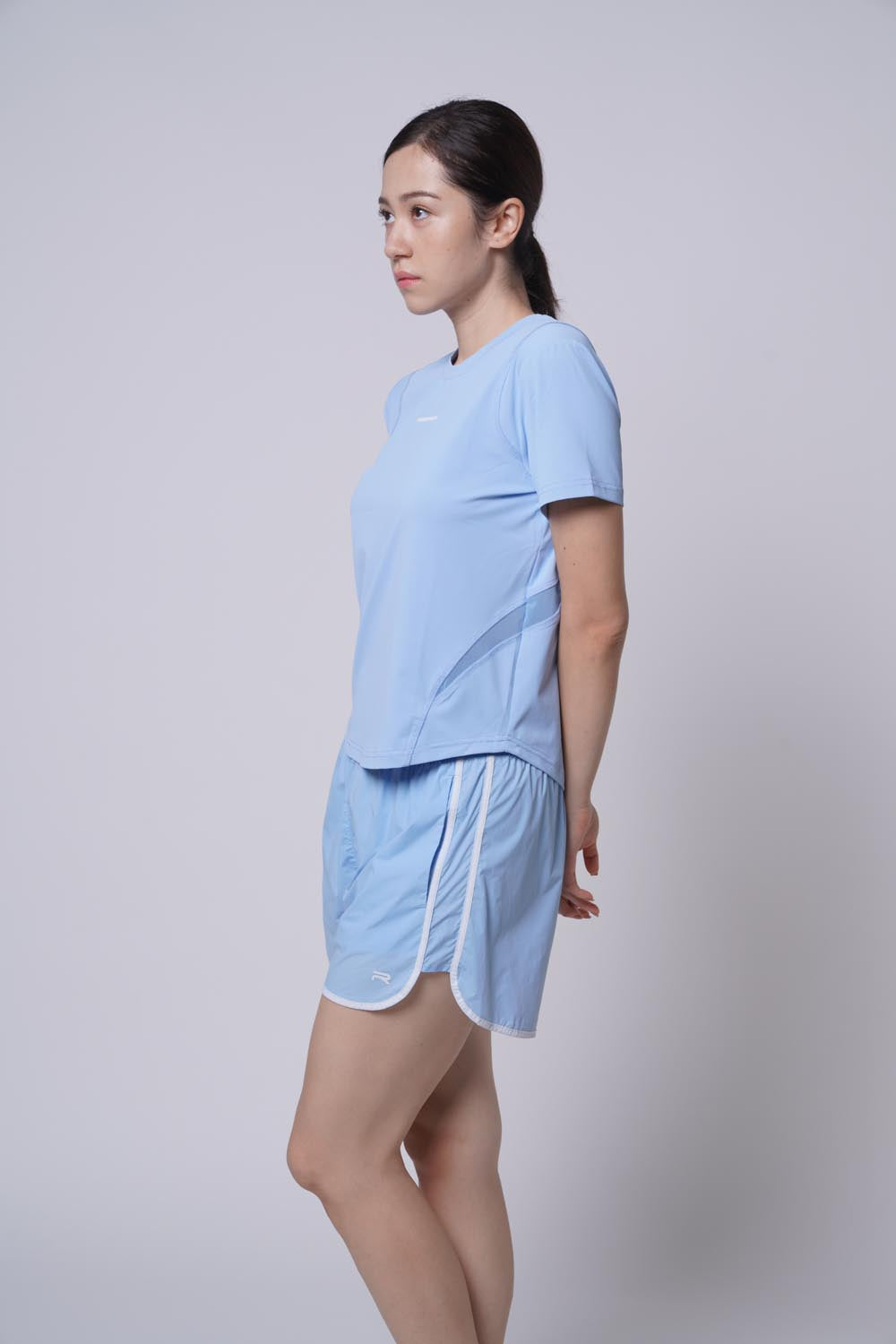 Asian female model looking away as she's posing while wearing a blue Ramsports Flow Panel Split-Hem Short and a blue shirt.