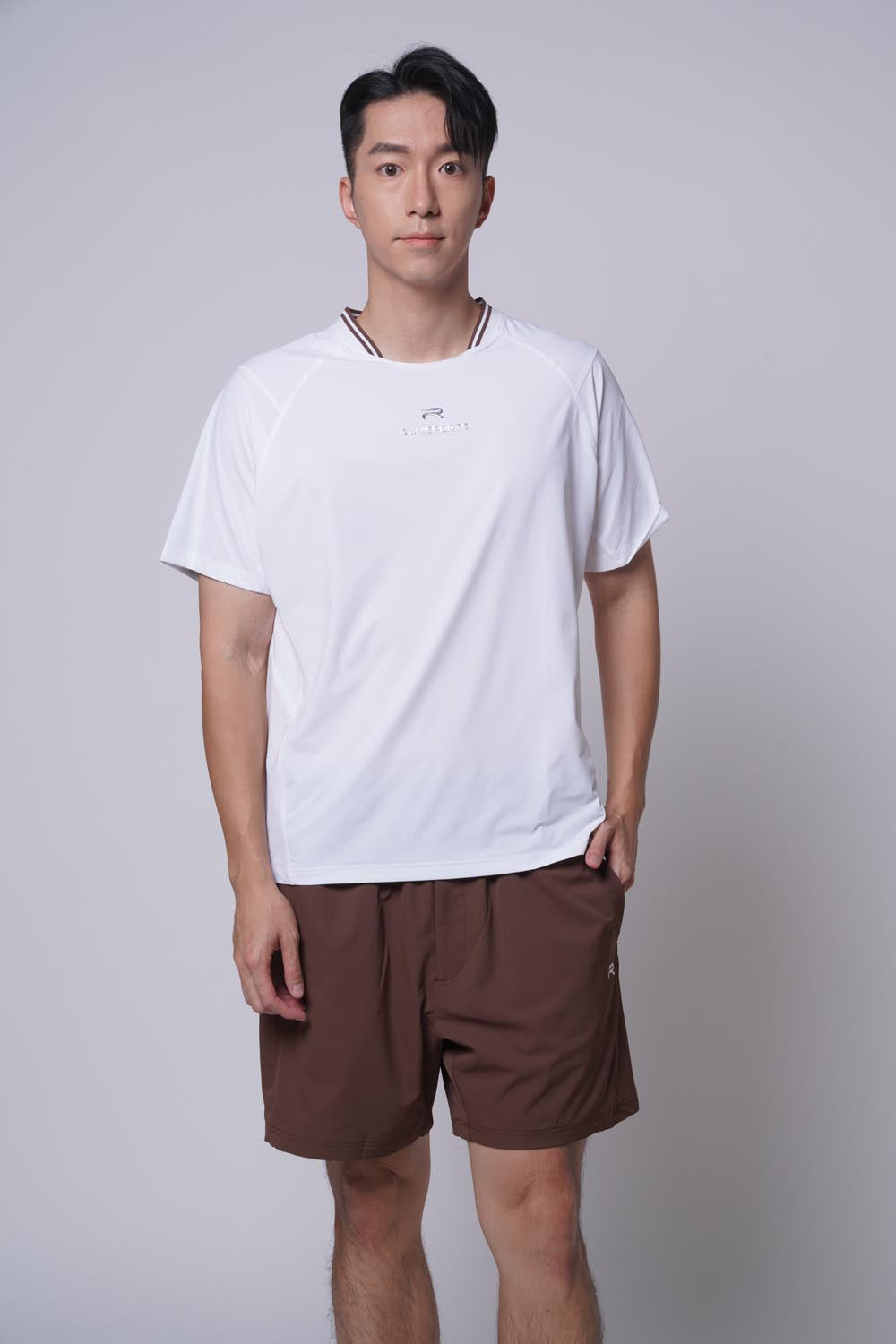 Asian male model standing sideways, with one hand on his pocket, wearing Ramsports Edge Line Raglan Tee in white with brown shorts