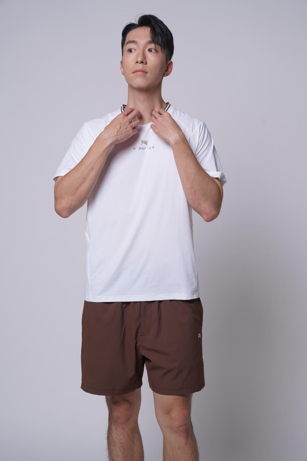 Male model standing sideways, hands on neck, wearing ramsports Edge Line Raglan Tee in white with brown shorts