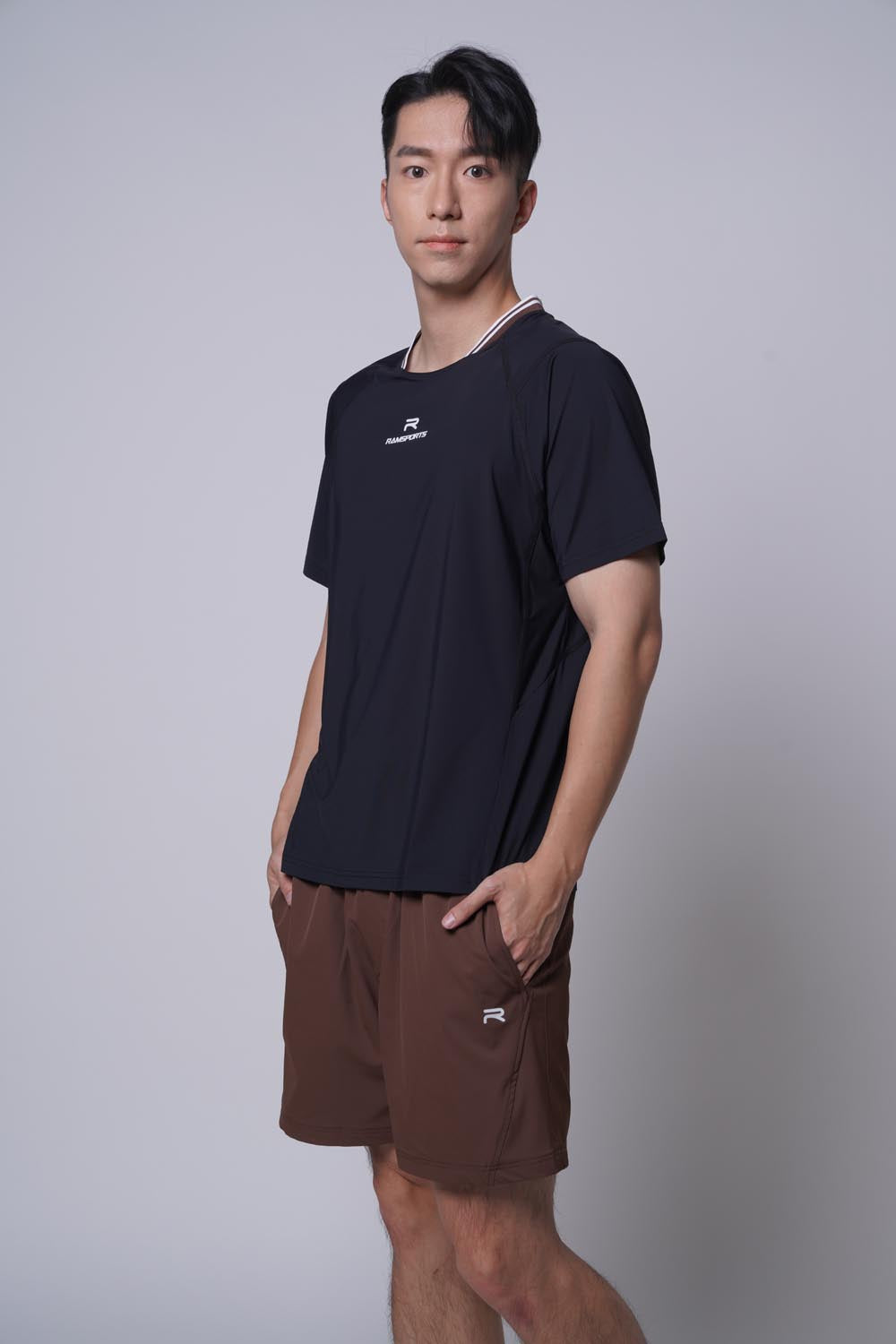 Asian male model facing sideways while looking at the camera, wearing ramsports Edge Line Raglan Tee in black with brown shorts
