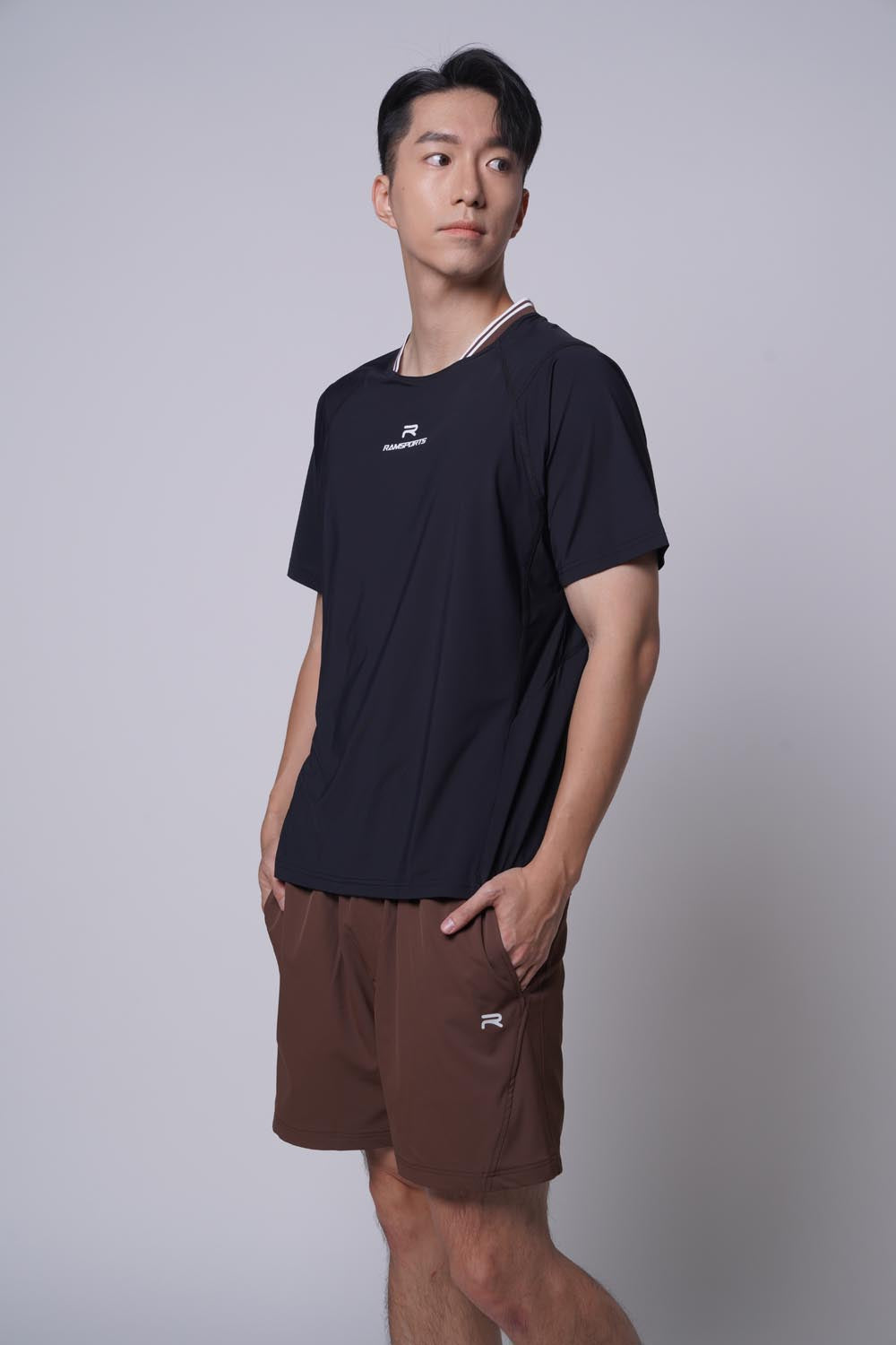 Asian male model standing sideways, looking away from the camera with both hands on pocket, wearing ramsports Edge Line Raglan Tee in black