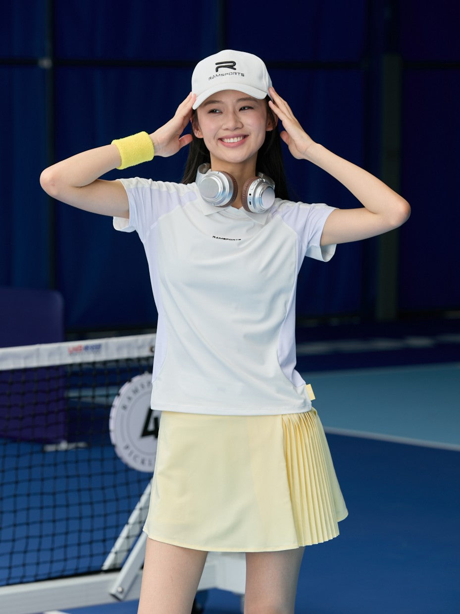 Asian female model wearing a yellow Ramsports AirFlow Pleated Skort and white shirt, posed as she's holding her white cap