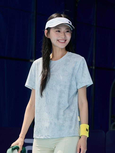 Smiling Asian female model wearing a gray Ramsports CoolDry Marble Print Tee, light yellow shorts, a white visor, and a yellow wristband
