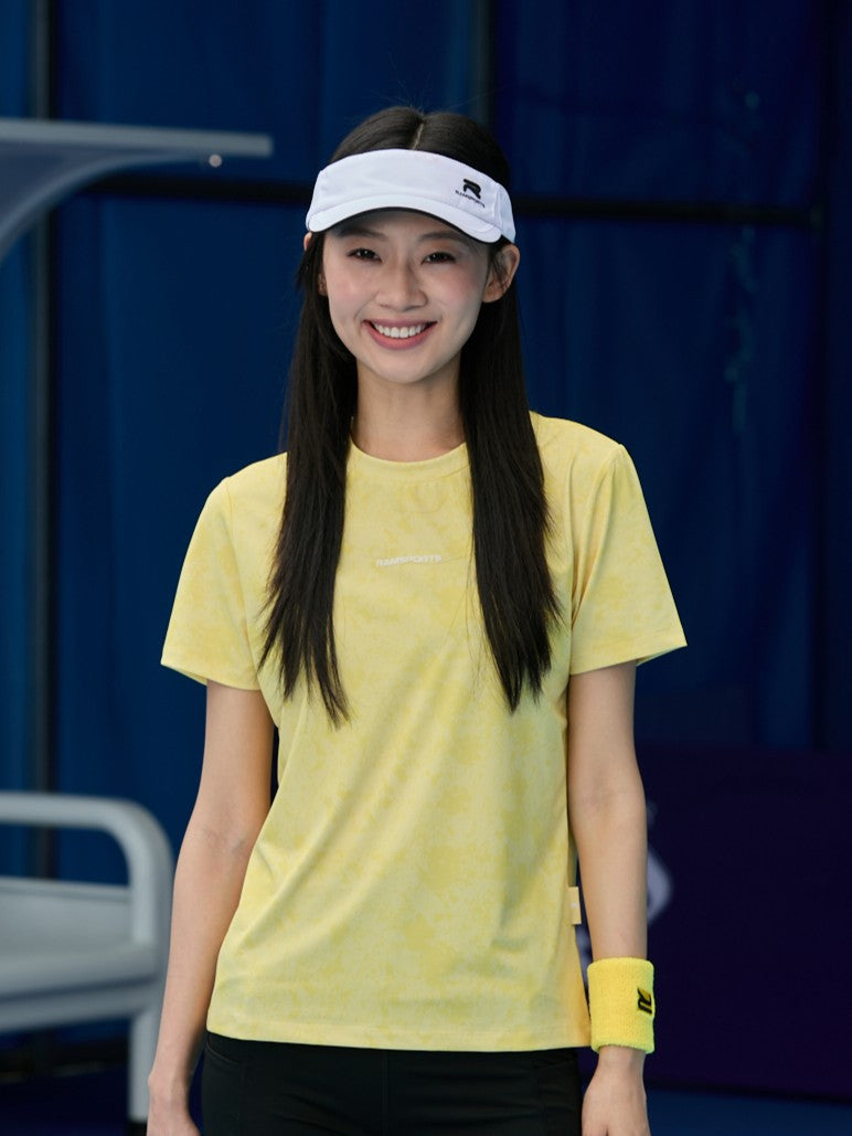 Smiling Asian female model wearing a yellow Ramsports CoolDry Marble Print Tee with black shorts, a yellow wristband, and a white visor