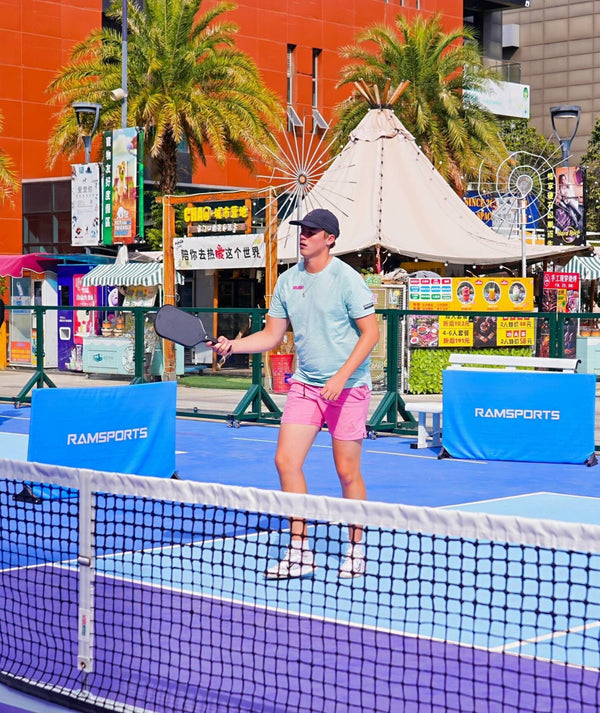 Western male player on the same court, appearing as the partner player or playing doubles, holding the Ramsports Ignis Pro Pickleball Paddle