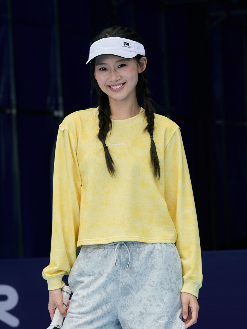 Smiling Asian female model wearing a yellow Ramsports EcoSoft Marble Print Crop Sweatshirt and gray shorts