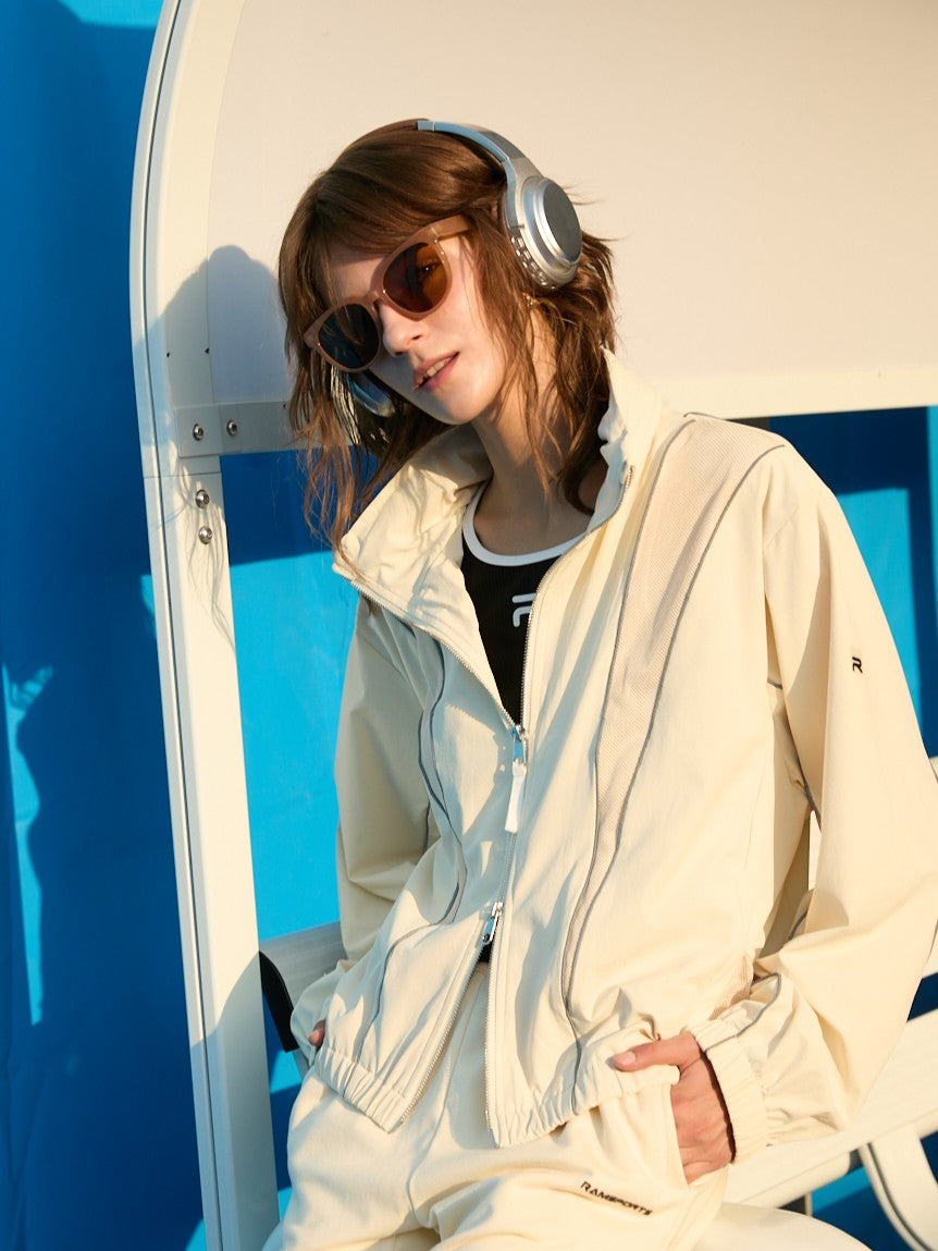 Female model wearing a khaki Ramsports FlexTek Block Jacket over a black top, slightly sitting or reclining
