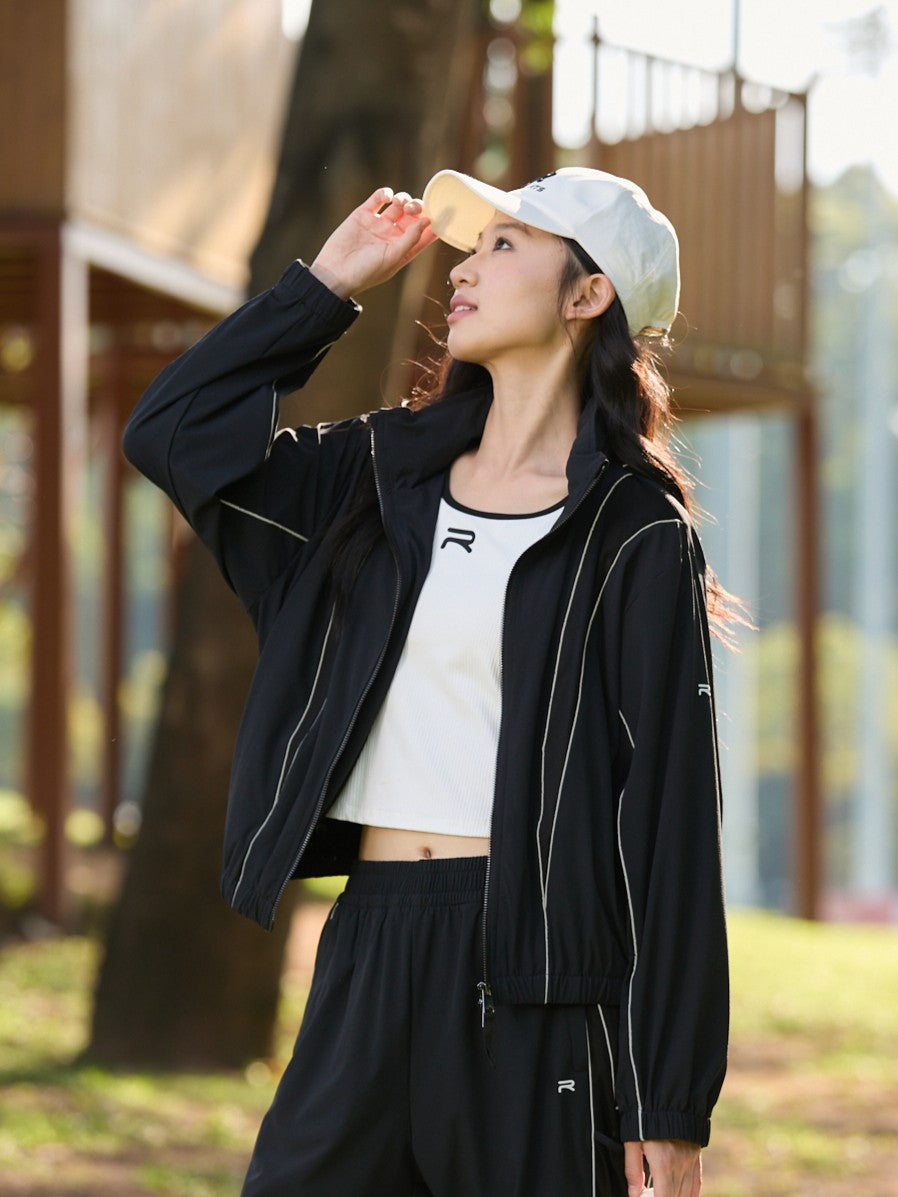 Asian female model wearing a black Ramsports FlexTek Block Jacket over a white top and black pants