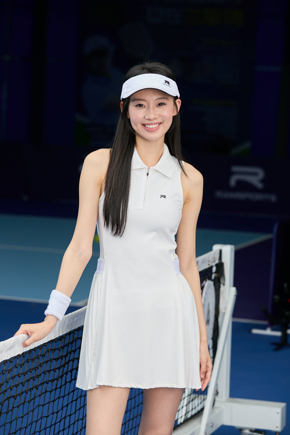 Asian female model wearing a white Ramsports FlexTek Court Dress, posing and holding the net