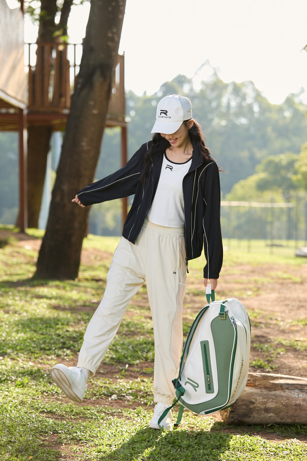 Smiling Asian female model playfully posing in khaki Ramsports FlexTek Motion Joggers, holding her backpack