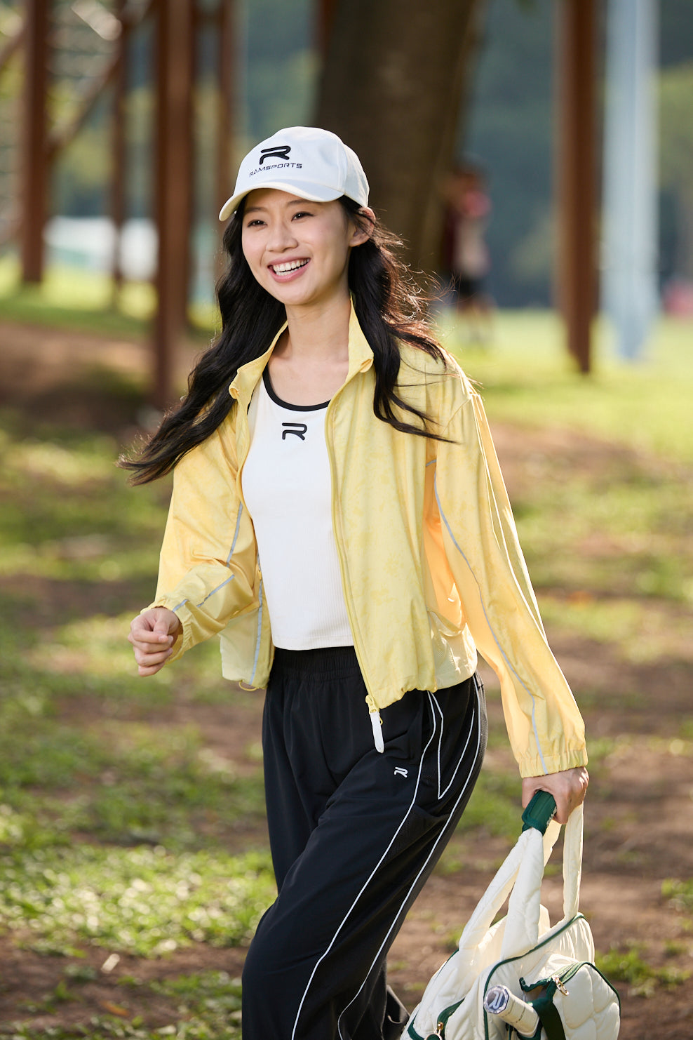 Smiling Asian female model wearing Ramsports FlexTek Motion Joggers in black with a white top and yellow jacket