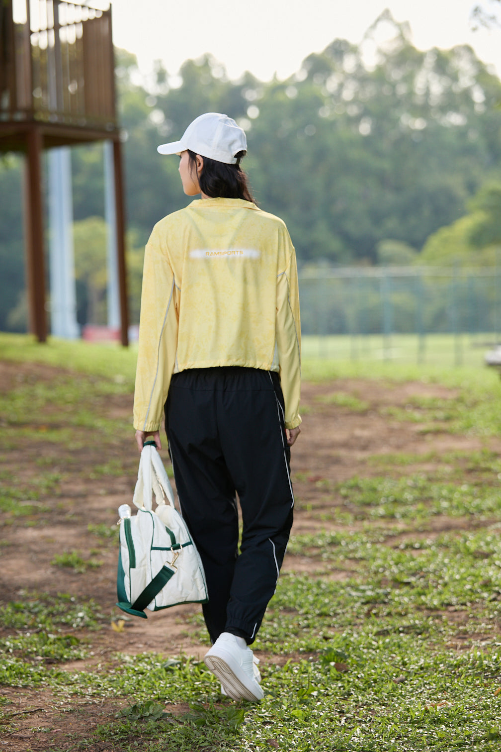 Asian female model facing away, wearing black Ramsports FlexTek Motion Joggers and holding a white cap