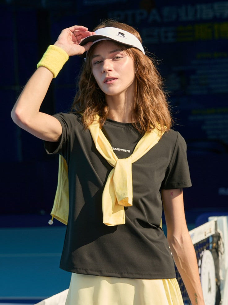 Female model holding the brim of her white hat, wearing a black Ramsports FlexTek Motion Tee paired with a yellow skort