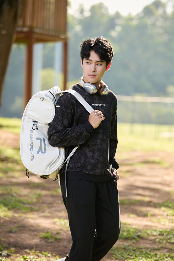 Asian male model dressed in all black, wearing the Ramsports LiteCarry Arctic Backpack with one strap over his shoulder
