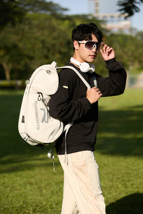 Asian male model in side view wearing the Ramsports LiteCarry Arctic Backpack with one strap, looking at the camera while holding his sunglasses in his other hand