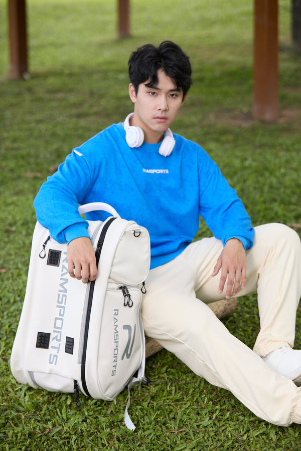Asian male model sitting with one hand resting on the Ramsports LiteCarry Arctic Backpack, both positioned on the ground.