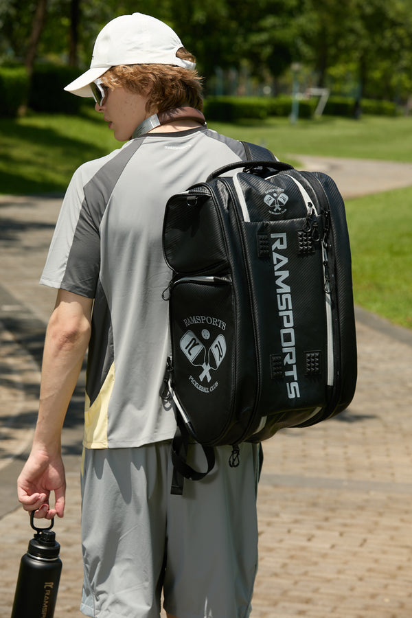 Male model facing away from the camera, wearing the Ramsports LiteCarry Court Backpack with one strap and holding a black Ramsports tumbler in the other hand