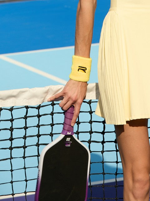 Cropped image of a female model wearing a sports wristband as she's holding the Ramsports Purple Express Pickleball Paddle right near or beside the net