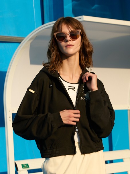 Female model wearing a black Ramsports EcoSoft Logo Hoodie, zipped in the middle over a white top
