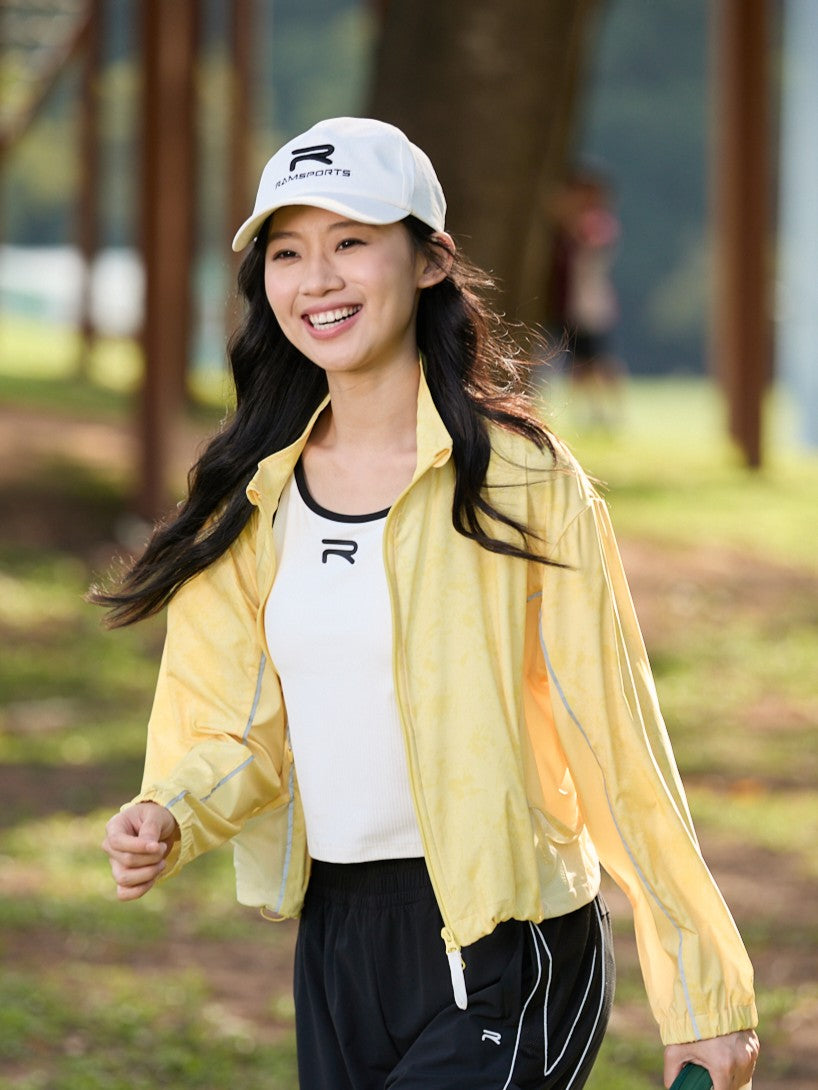 Smiling Asian female model in motion, wearing a yellow Ramsports FlexTek Marble Print Jacket over a white top and black pants