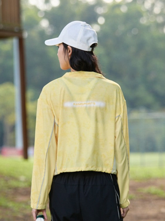 Smiling Asian female model facing away, wearing a yellow Ramsports FlexTek Marble Print Jacket over a white top and black pants