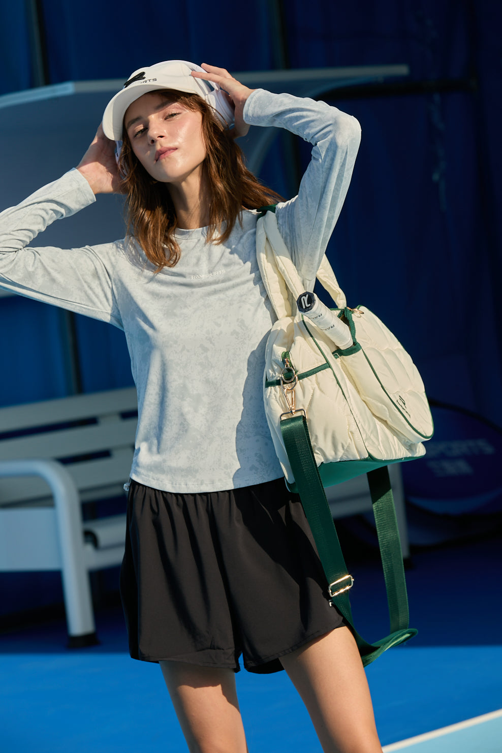 Female model holding headphones over white cap, wearing Ramsports FlexTek Pace Shorts in black and carrying a beige-green bag