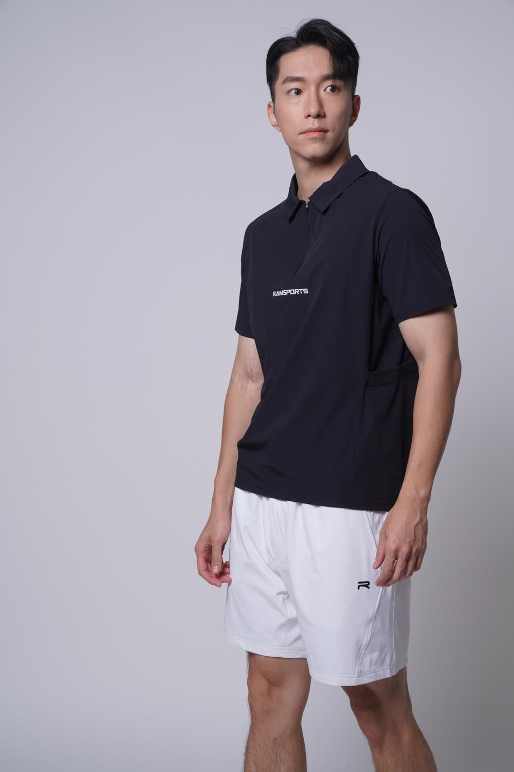 Asian male model standing sideways, looking away at the camera  wearing of Ramsports MatchDay Core Short in white and a black top