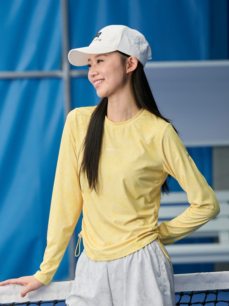 Asian female model looking away, wearing a yellow Ramsports CoolDry Marble Print Long-Sleeves Tee and gray shorts, slightly holding the net