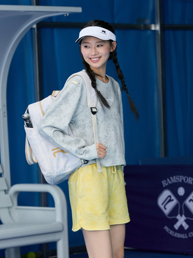 Smiling Asian model wearing yellow Ramsports EcoSoft Marble Print Shorts, posed sideways with a backpack