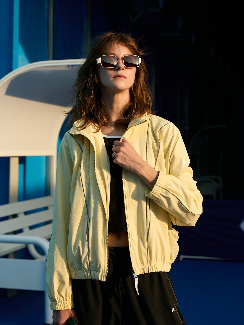 Female model wearing a yellow Ramsports FlexTek Block Jacket with black joggers as she's holding her jacket
