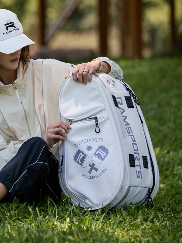 Female model sitting on the grass, trying to open a pocket of the Ramsports LiteCarry Arctic Backpack